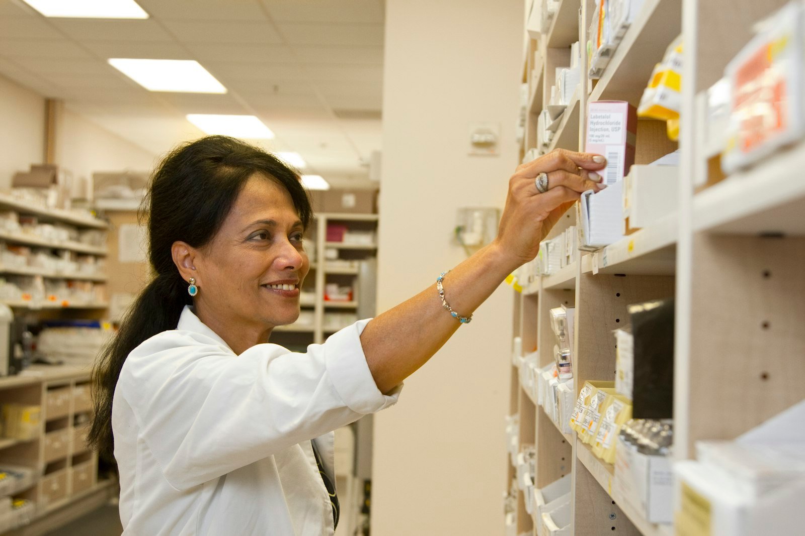 Pharmacien en blouse blanche prenant une boîte de médicaments en rayon